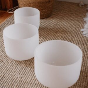 three white crystal sound bowls on woven carpet