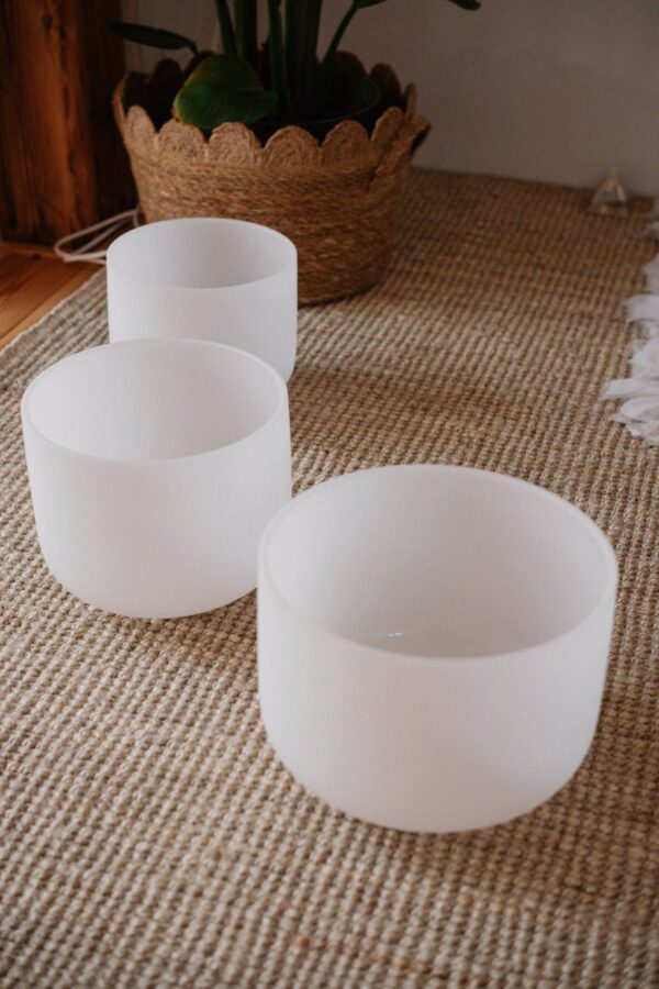 three white crystal sound bowls on woven carpet
