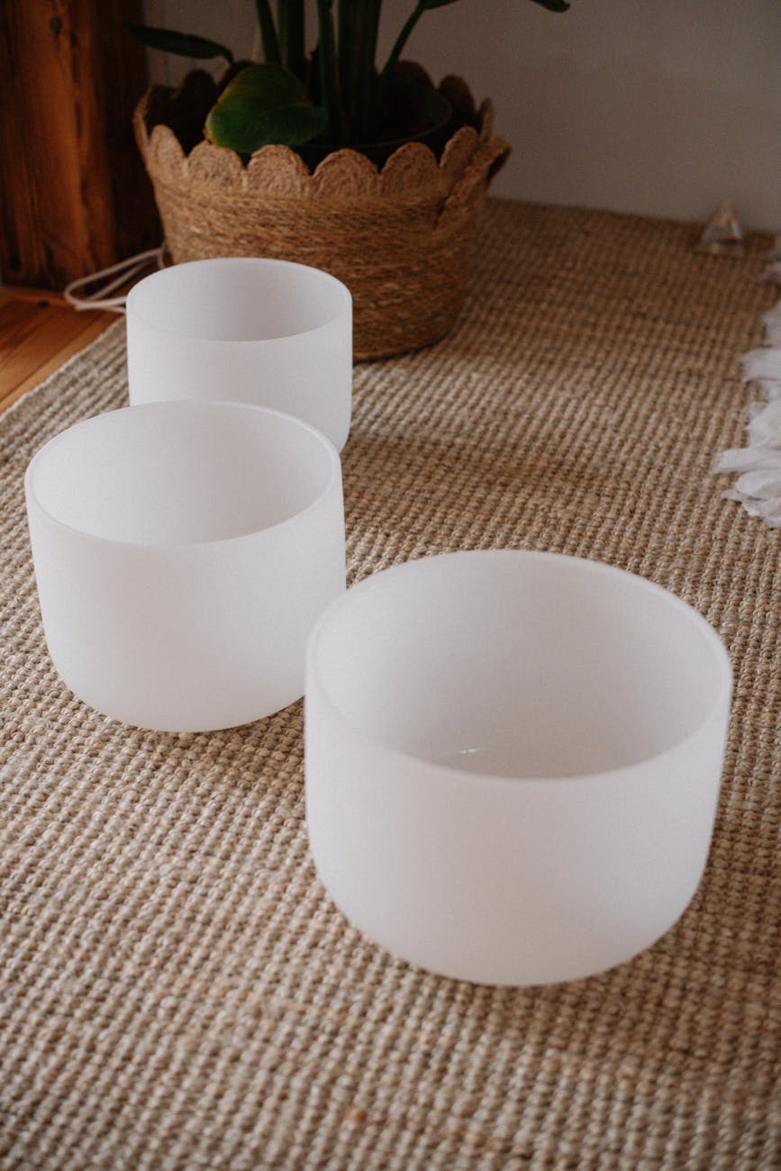 three white crystal sound bowls on woven carpet